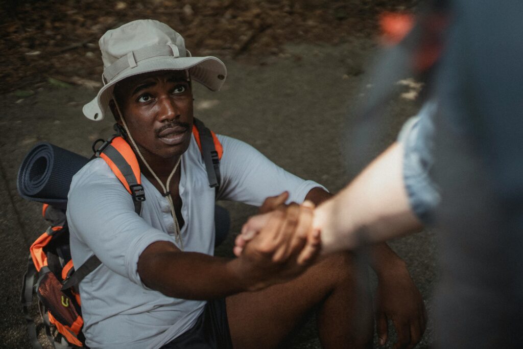 A hiker in summer gear receiving help from a companion in an outdoor setting.